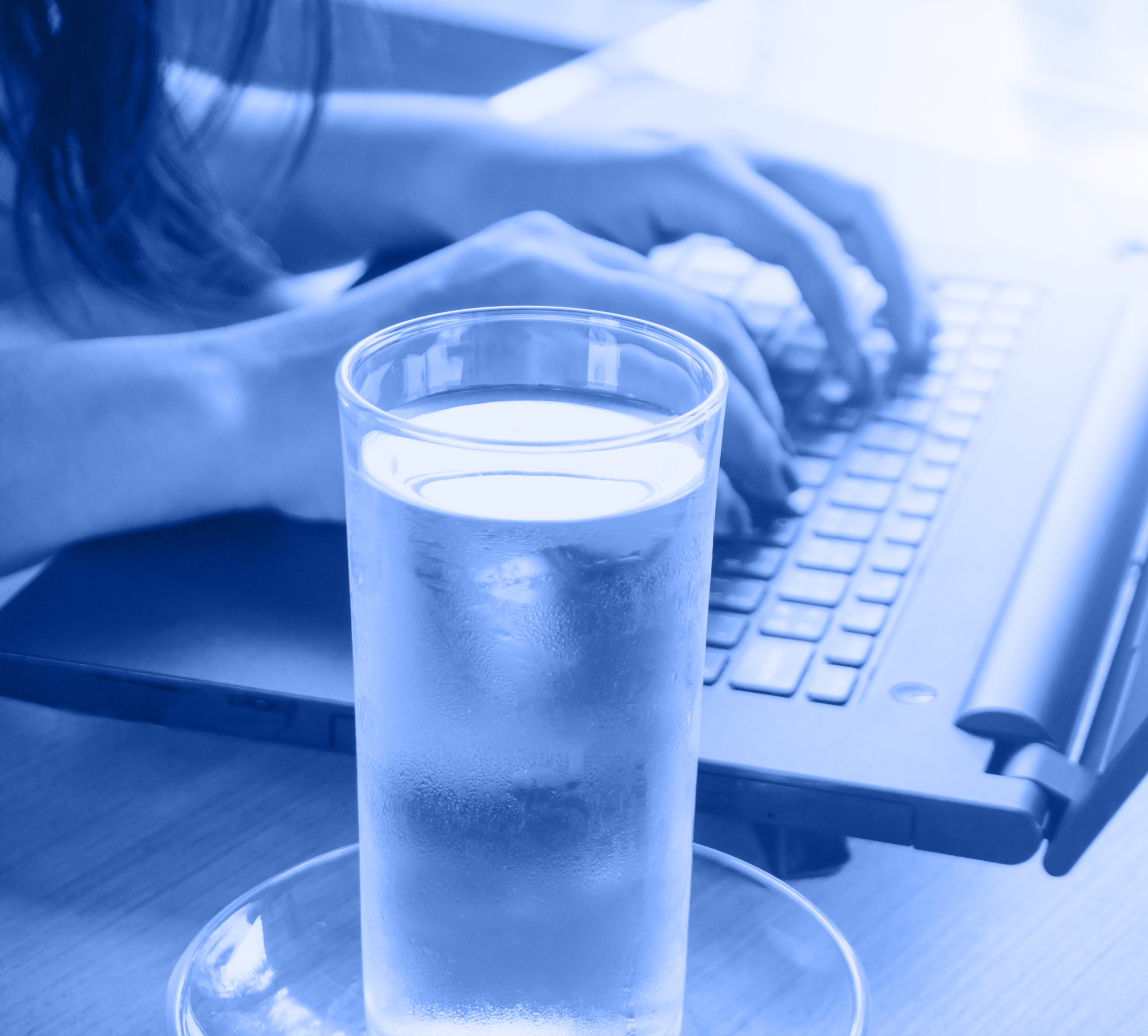 Woman typing with glass of water on the side
